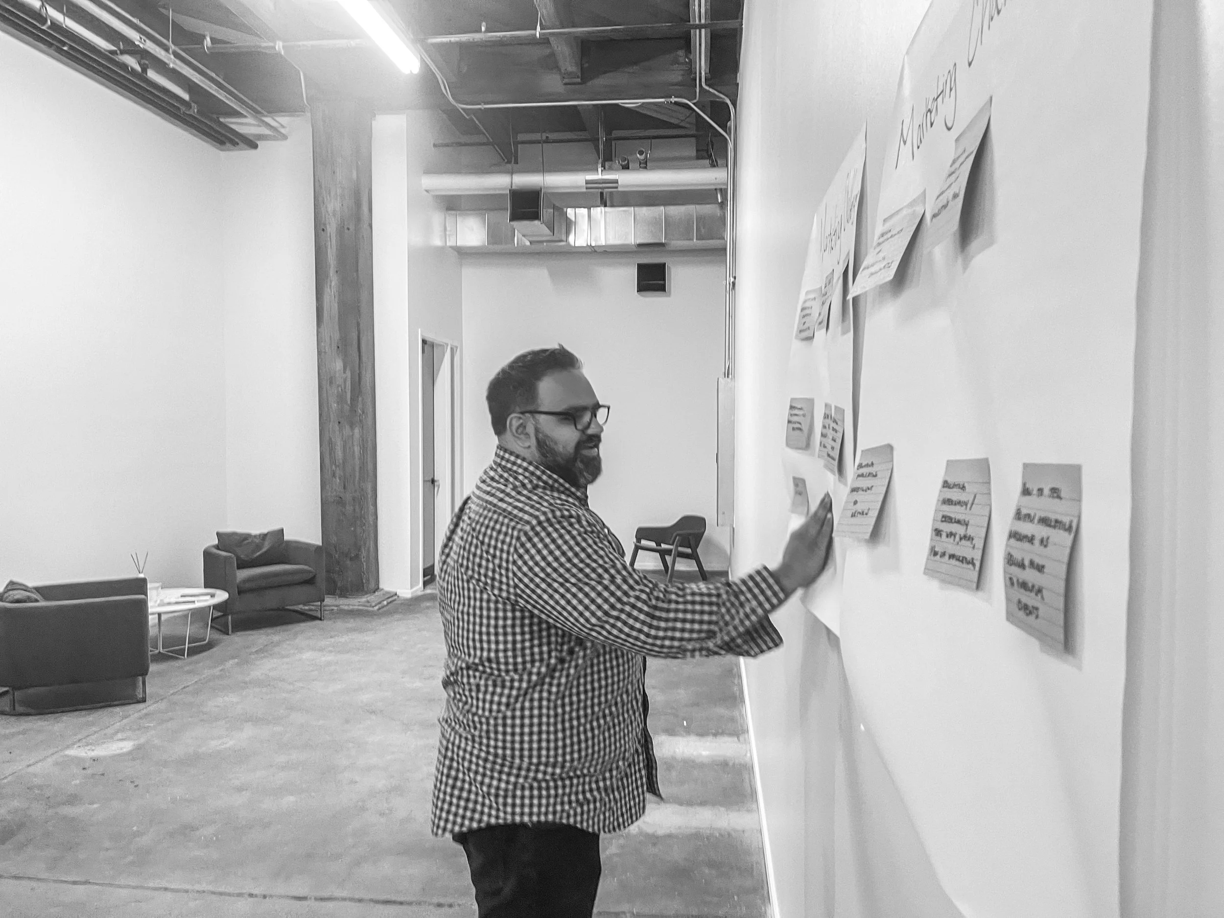 Communications Strategist Raj Lulla conducts a brainstorming session, placing sticky notes on large sticky pages in a renovated industrial building.