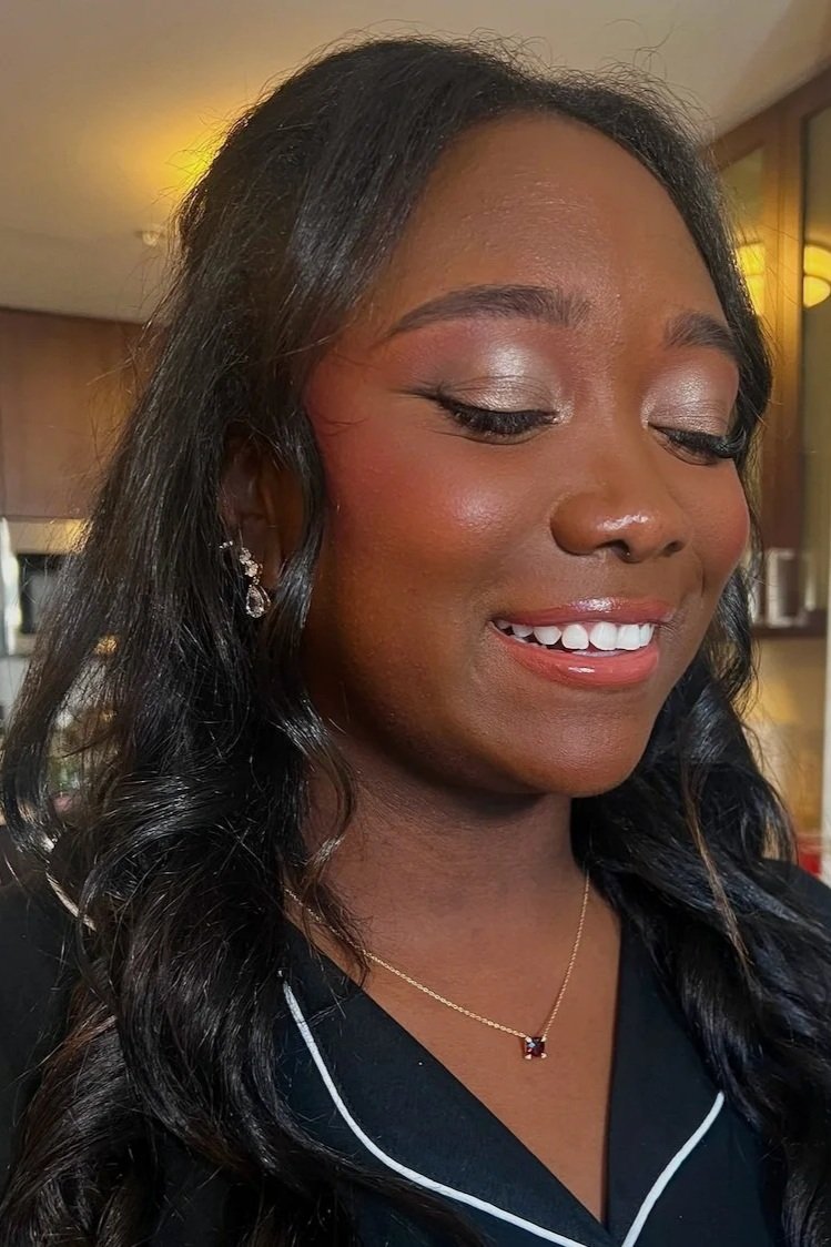Smiling woman with dark hair, wearing jewelry and makeup, indoors.