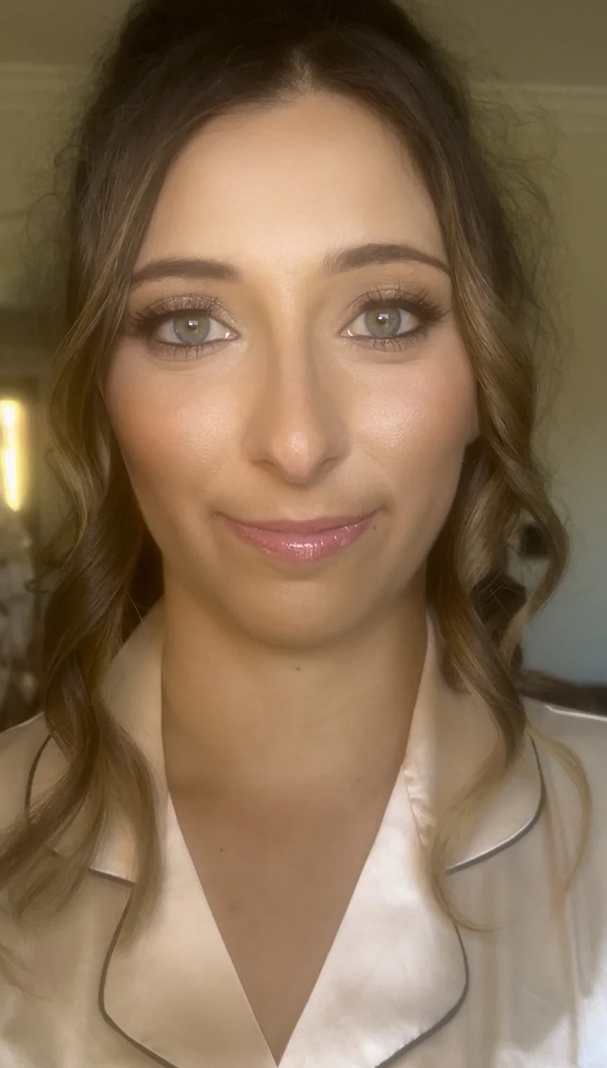 Close-up image of a young woman with wavy brown hair, blue eyes, light makeup, and wearing a silk pajama top with black piping.