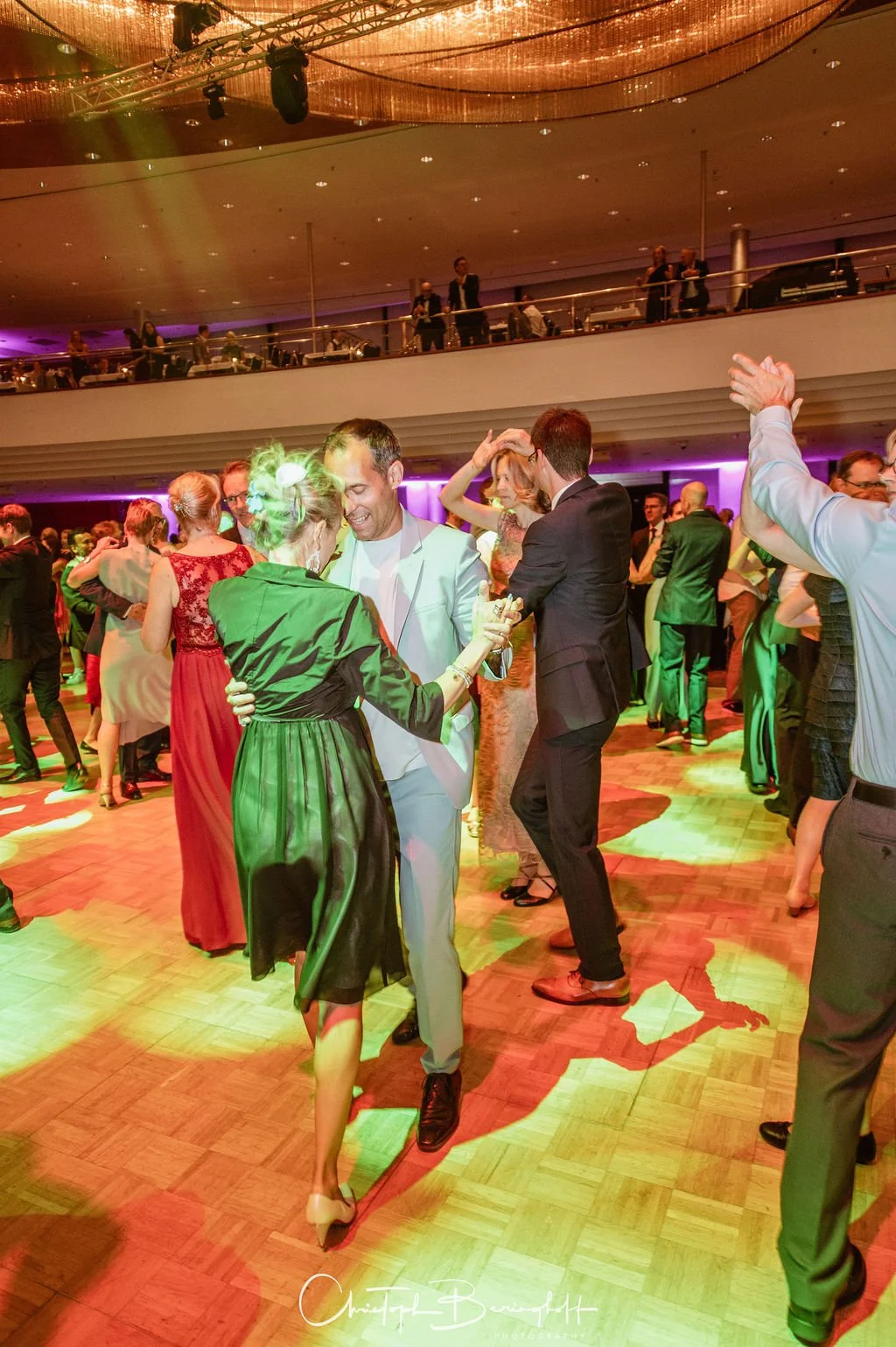 Menschen tanzen auf einer Party im eleganten Ambiente mit buntem Licht, auf einem Holzparkett im Veranstaltungsraum.