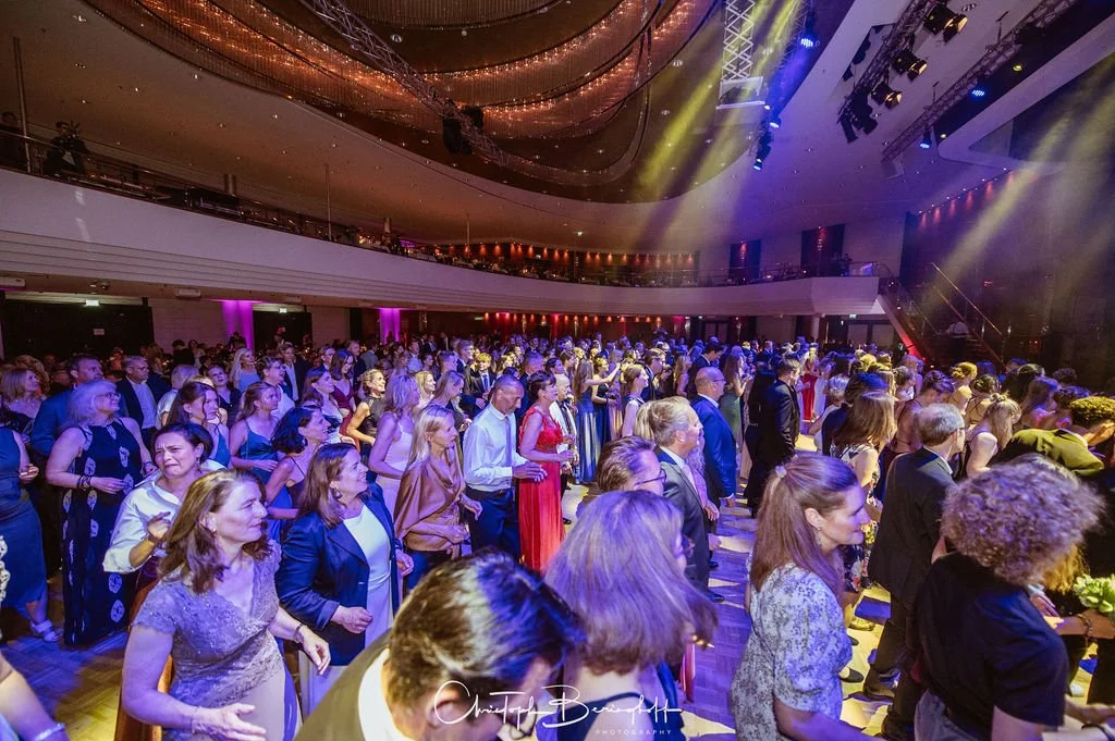 Menschen bei einer Veranstaltung im Ballroom, tanzend und zuschauend, mit buntem Licht und dekoriertem Raum.