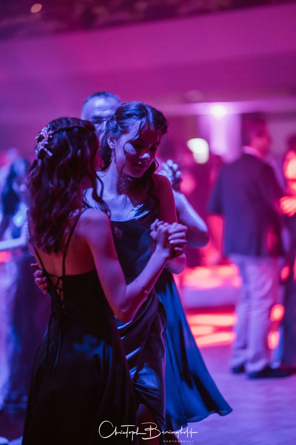 Zwei Frauen tanzen auf einer Party im dunklen Raum mit buntem Licht.
