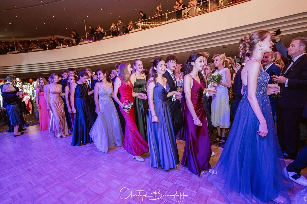 Junge Frauen in elegante Abendkleider stehen in einer Linie bei einer formellen Veranstaltung in einem großen Veranstaltungsraum.