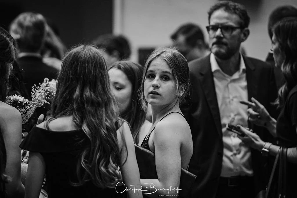Junge Frau in schwarzem Kleid unter Menschenmenge, die an einem sozialen Event teilnehmen.