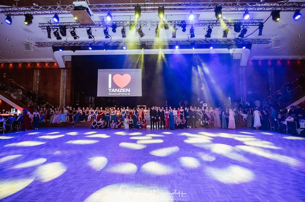 Tanzveranstaltung mit vielen Tänzern im Festsaal, auf der großen Leinwand steht 'Ich liebe Tanzen'.