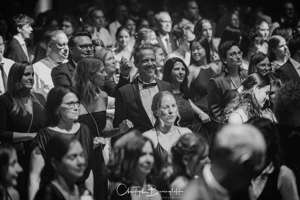 Menschen bei einer formellen Veranstaltung, einige lachen und applaudieren, alle in eleganter Kleidung, schwarz-weiß Fotografie