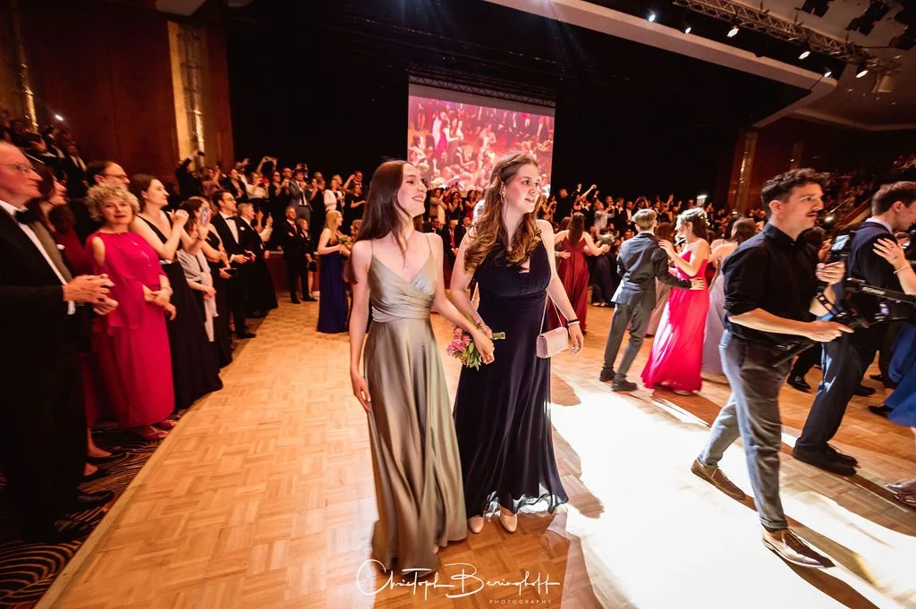 Menschen in eleganter Abendgarderobe bei einer Gala oder Ball, tanzend und applaudierend in einem prachtvollen Saal.