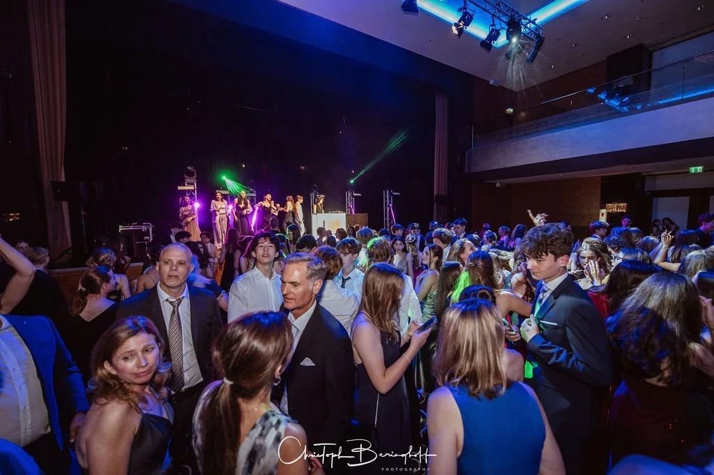 Menschen tanzen und feiern auf einer Party mit einer Bühne und Musik im Hintergrund.