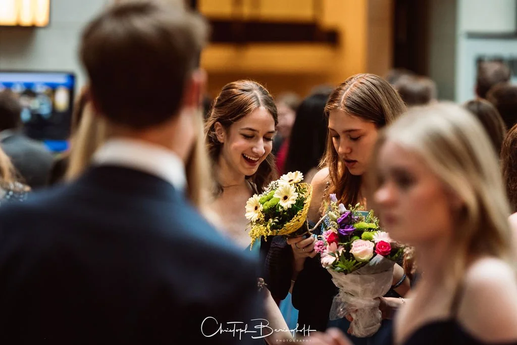 Menschen bei einer Feier, Frauen mit Blumensträußen im Gespräch