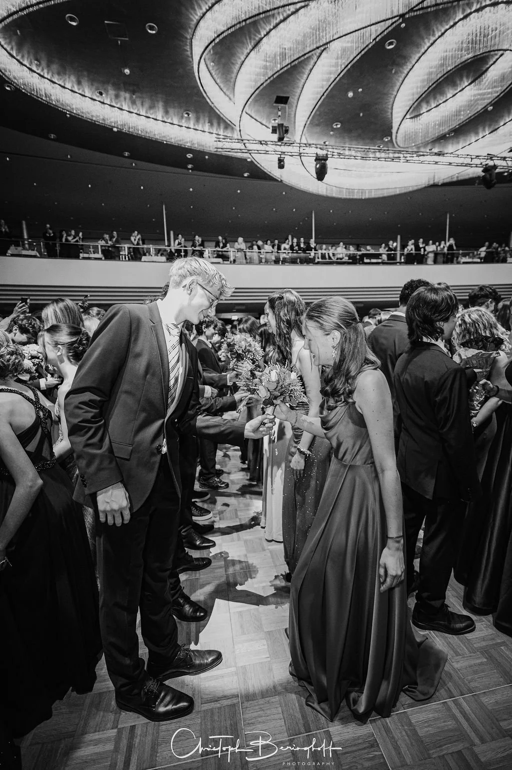 Menschen bei einem Gala-Empfang, die Blumen überreichen, im eleganten Abendkleid und Anzug, in einem festlichen Veranstaltungsraum.
