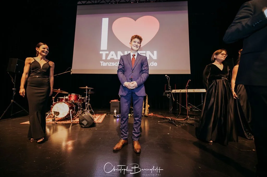 Menschen auf einer Bühne bei einer Veranstaltung, im Hintergrund eine Leinwand mit einem Herz und dem Text 'I ❤️ TANSEN'.