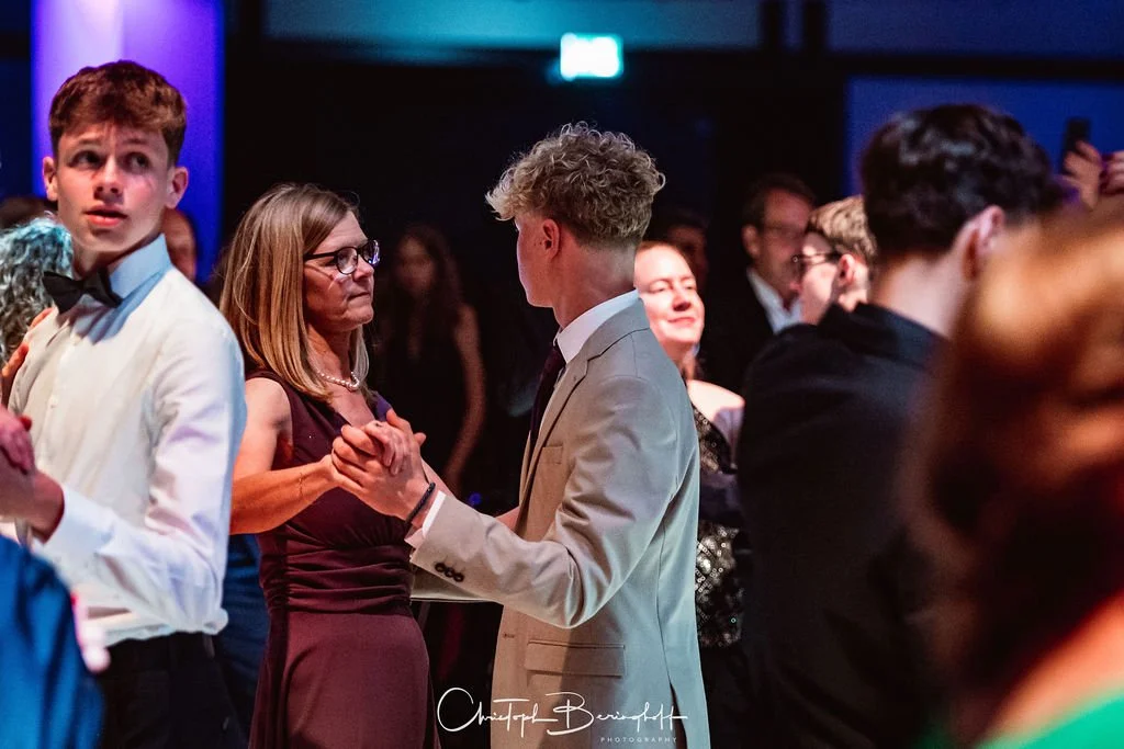 Menschen tanzen auf einer Party oder Hochzeit im Abendlicht, umgeben von weiteren Gästen.
