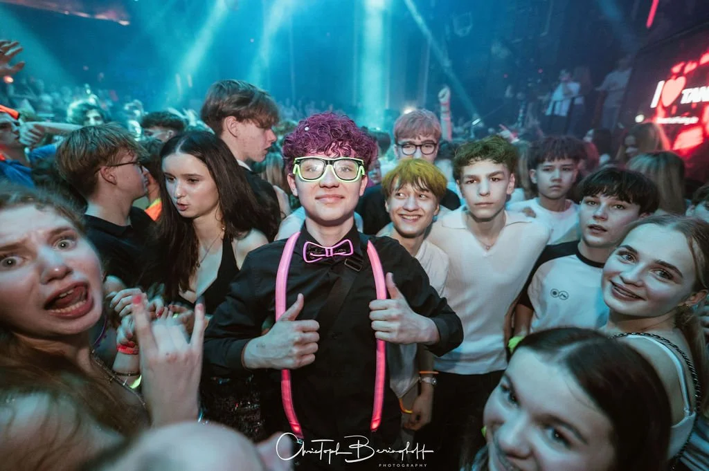 A group of teenagers at a party in a club with colorful lights.