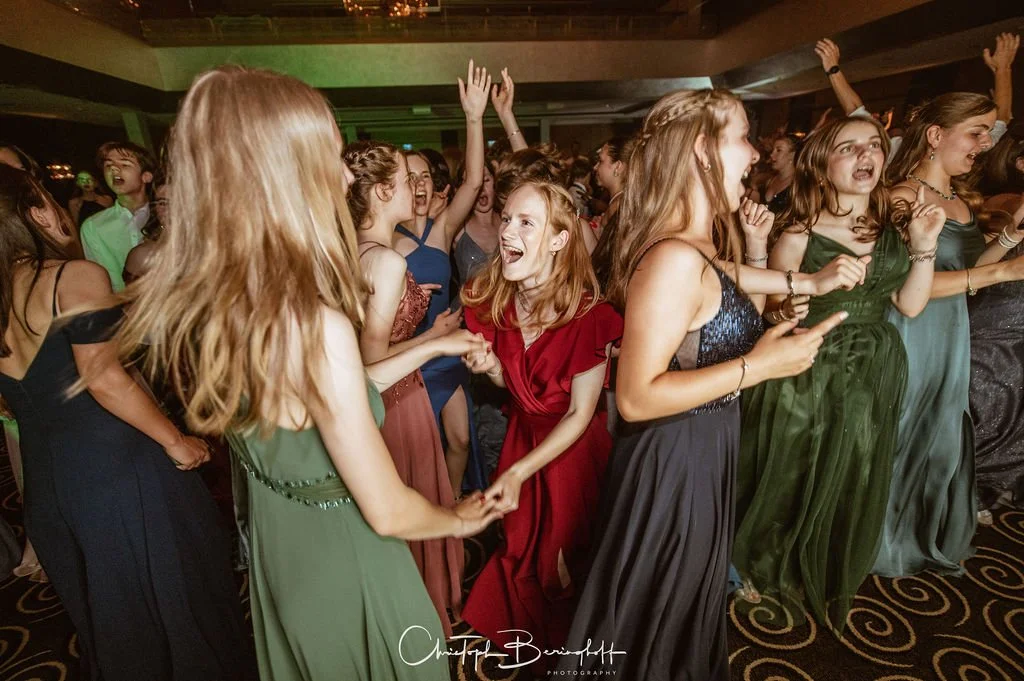 Eine Gruppe junger Frauen tanzt und lacht auf einer Party in eleganten Abendkleidern.