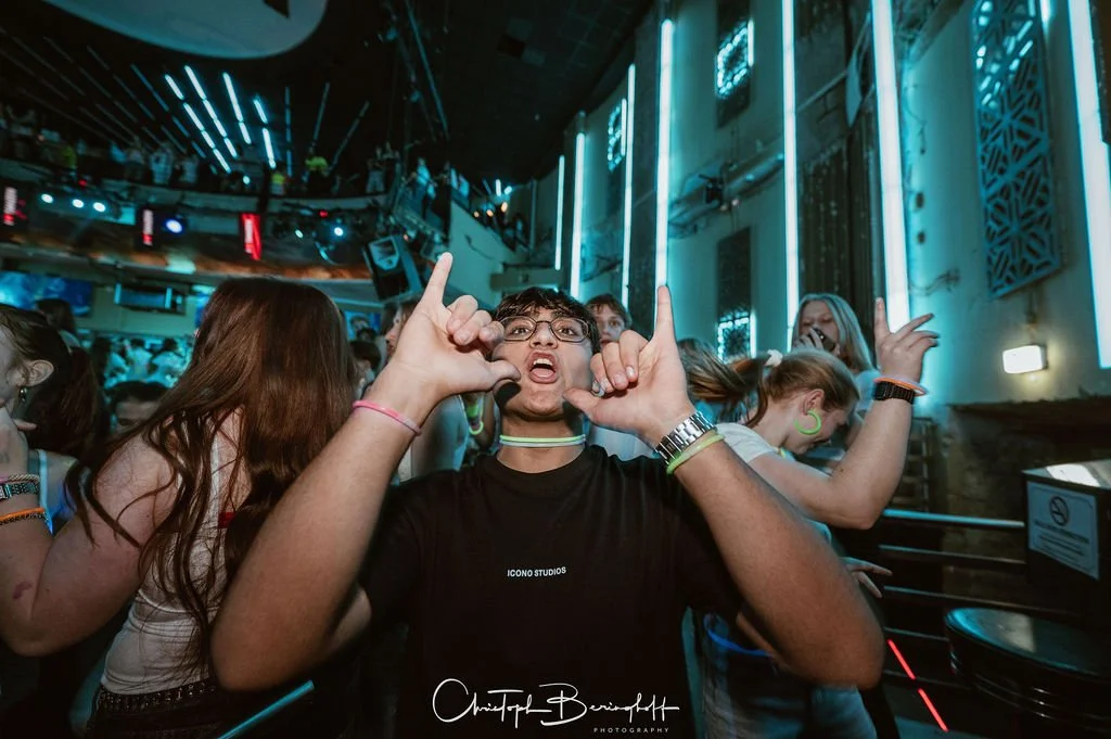 People are partying in a dark club lit by blue lights; the atmosphere is cheerful and energetic.