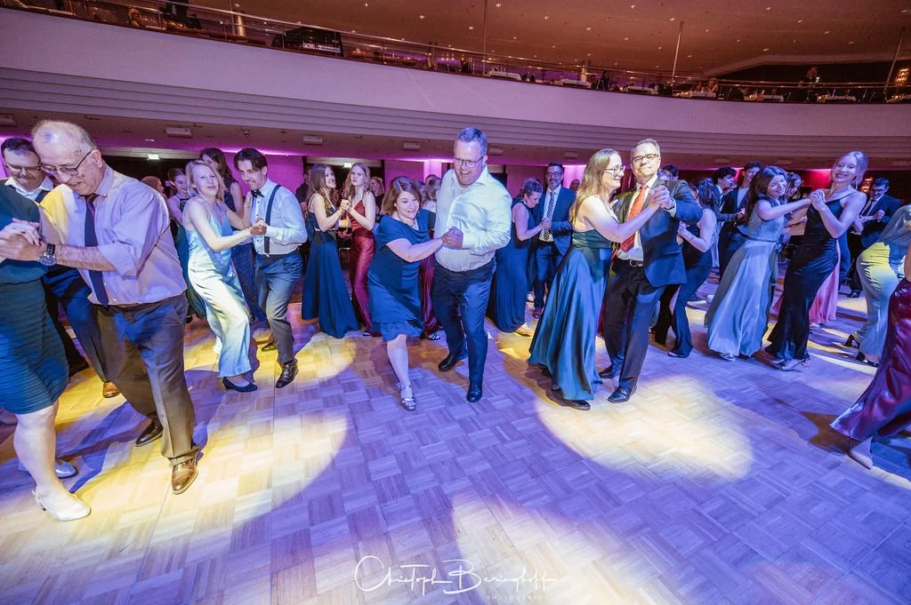 Menschen tanzen in einem großen Saal bei einer Veranstaltung mit bunter moderner Beleuchtung.