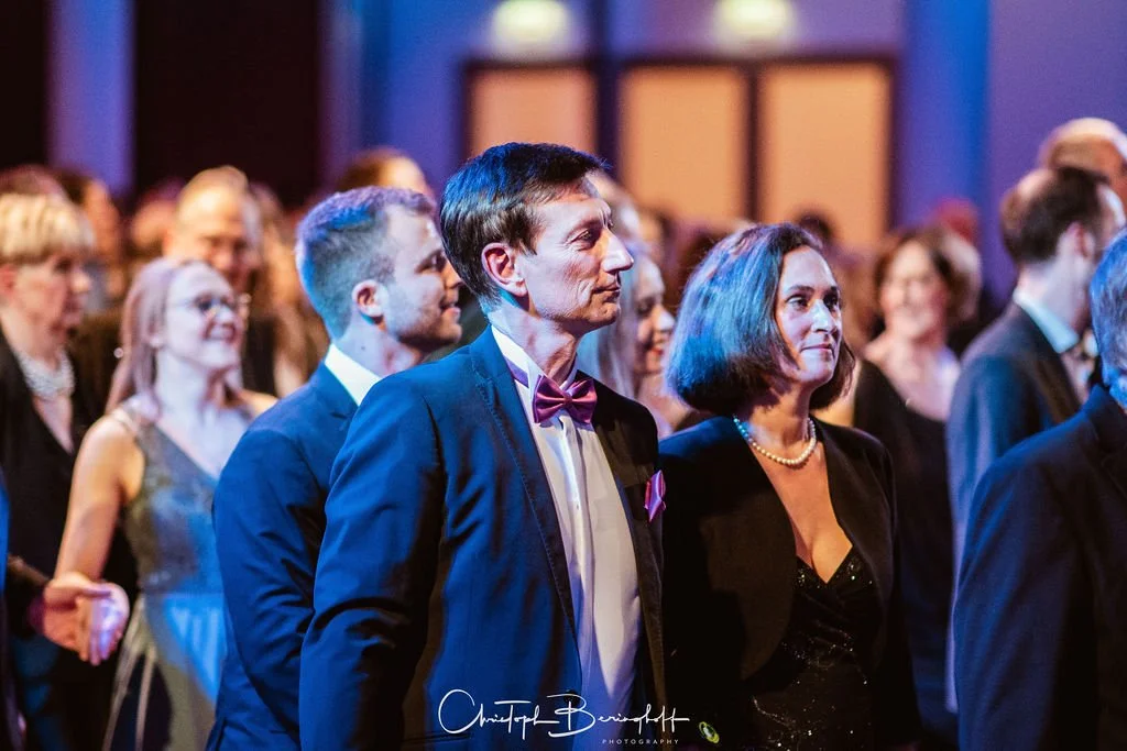 Menschen in eleganter Kleidung bei einer formellen Veranstaltung, die einen Vortrag oder eine Zeremonie beobachten.