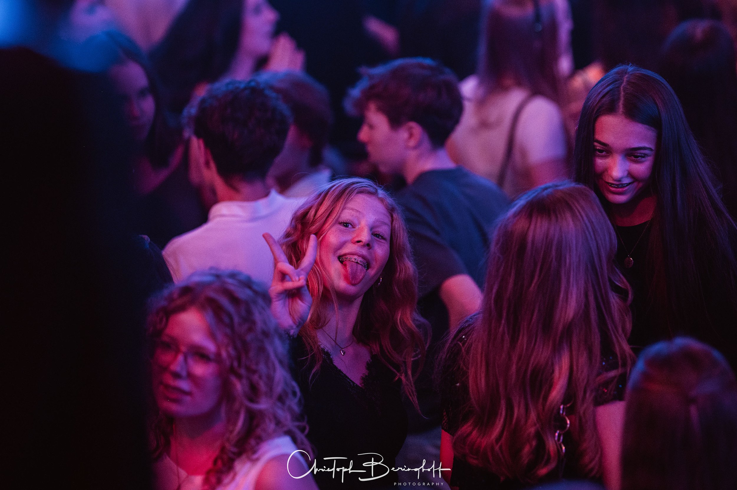 Menschen, die bei einer Party im Dunkeln tanzen, einige lächeln und lachen, mit bunten Lichtern im Hintergrund.