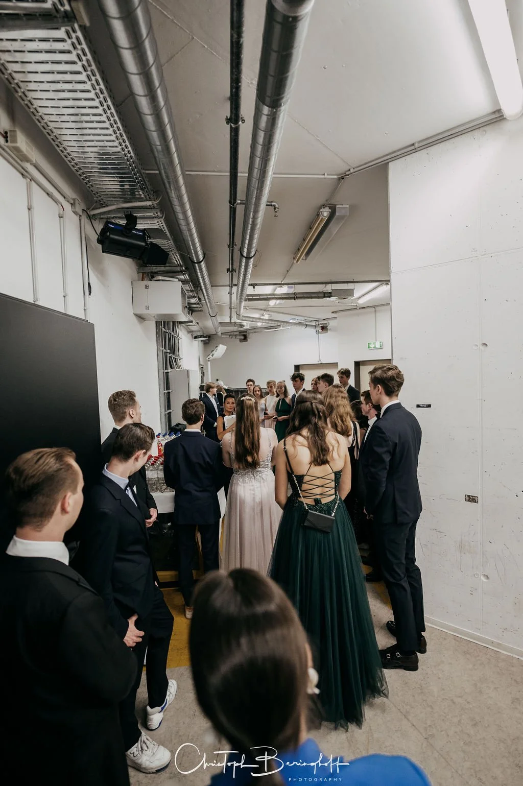 Gruppe von jungen Menschen, die formell gekleidet in einem Flur warten, möglicherweise bei einer Veranstaltung oder Hochzeit.