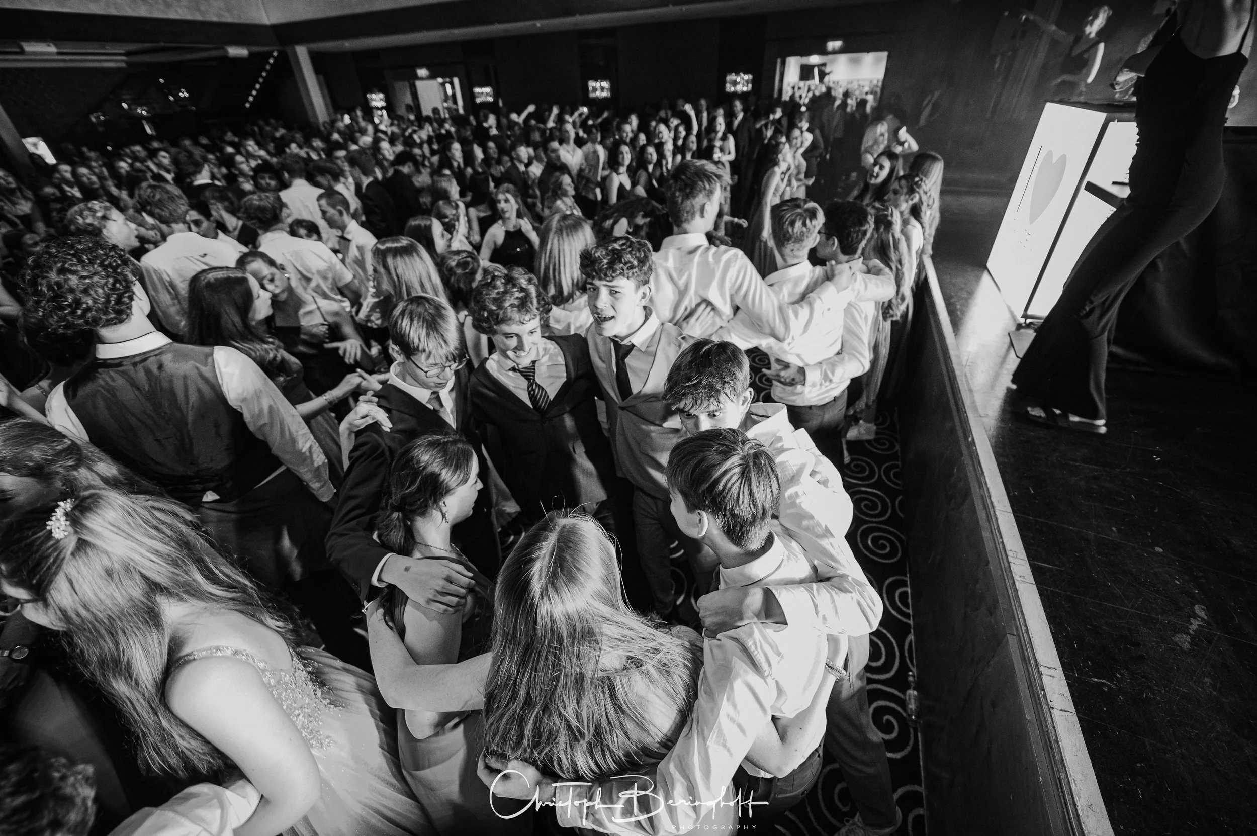 Viele Jugendliche tanzen und feiern auf einer Party oder einem Event in einem großen Saal, mit Blick auf die Tanzfläche und verwandten Aktivitäten.