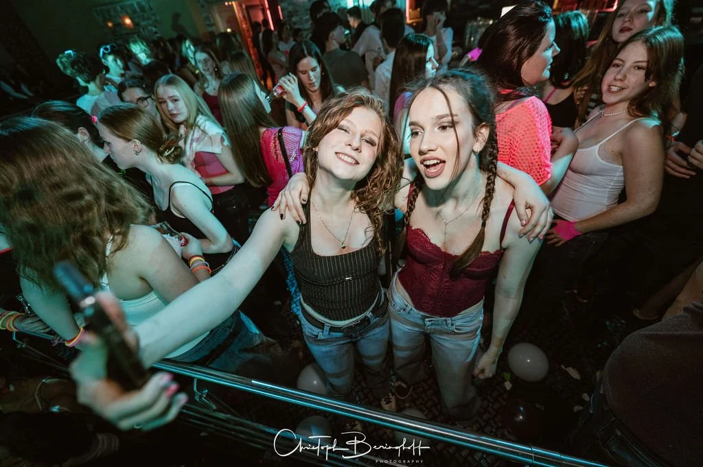 Young women are dancing and partying at a nightclub, surrounded by other partygoers on the dance floor.