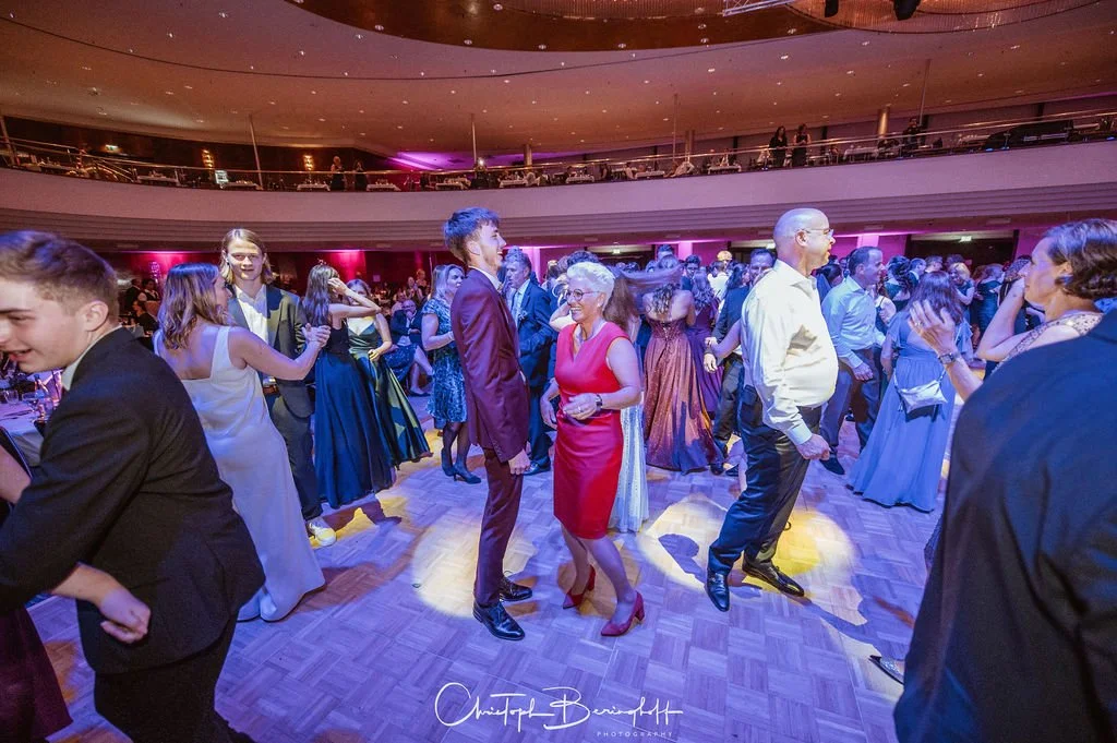 Menschen tanzen auf einer festlich dekorierten Tanzfläche, im Hintergrund ein zweiter Stock mit Sitzplätzen bei einer Gala oder Hochzeit.