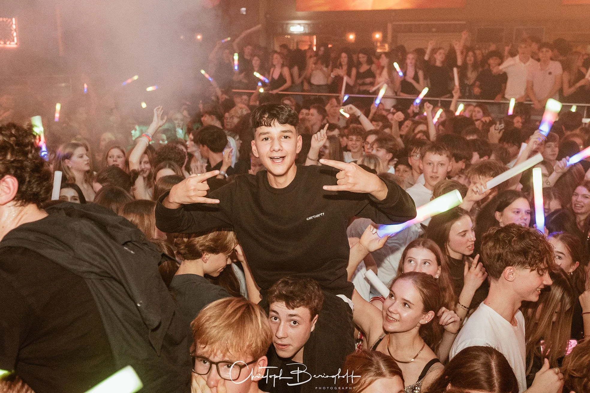 Junge bei einem Konzert mit leuchtenden Gegenständen in der Hand, mittendrin in einer Menschenmenge, die feiert.