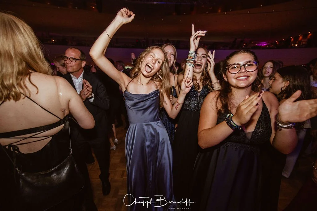 Menschen feiern auf einer Party, tanzen und lachen im dunklen Raum mit buntem Licht.