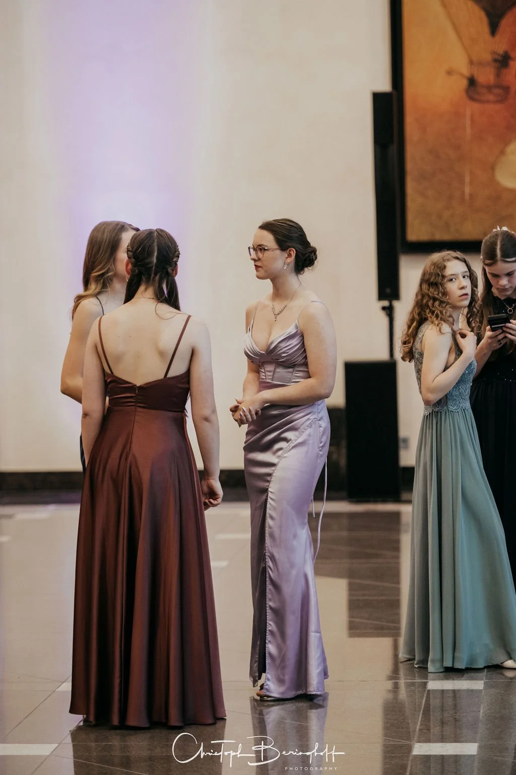 Fünf Frauen in eleganten Abendkleidern stehen in einem Raum bei einer Veranstaltung.