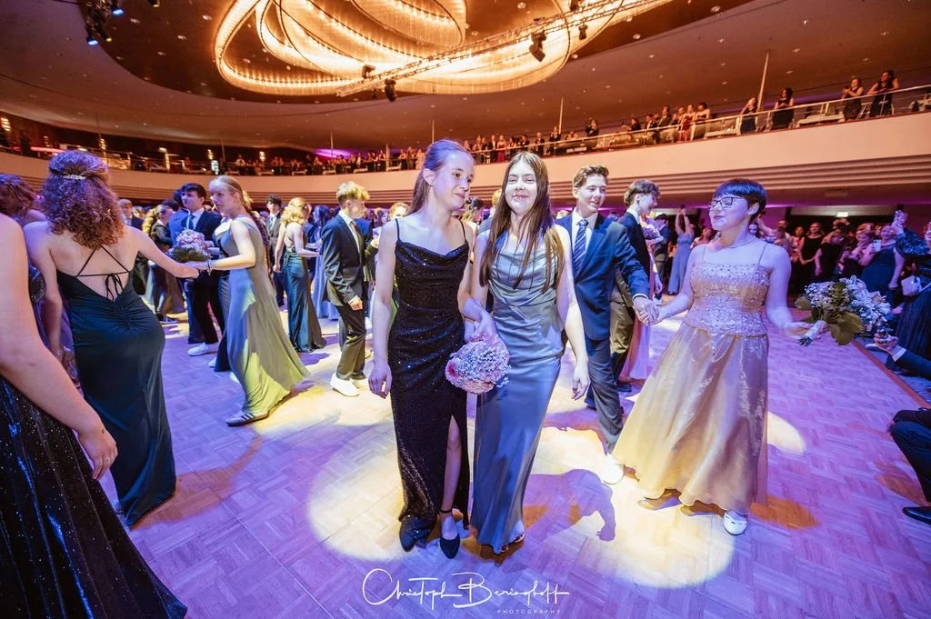 Jugendliche beim Ball oder Tanzveranstaltung im festlichen Abendkleid auf einem Tanzparkett mit aufwändiger Deckenbeleuchtung.