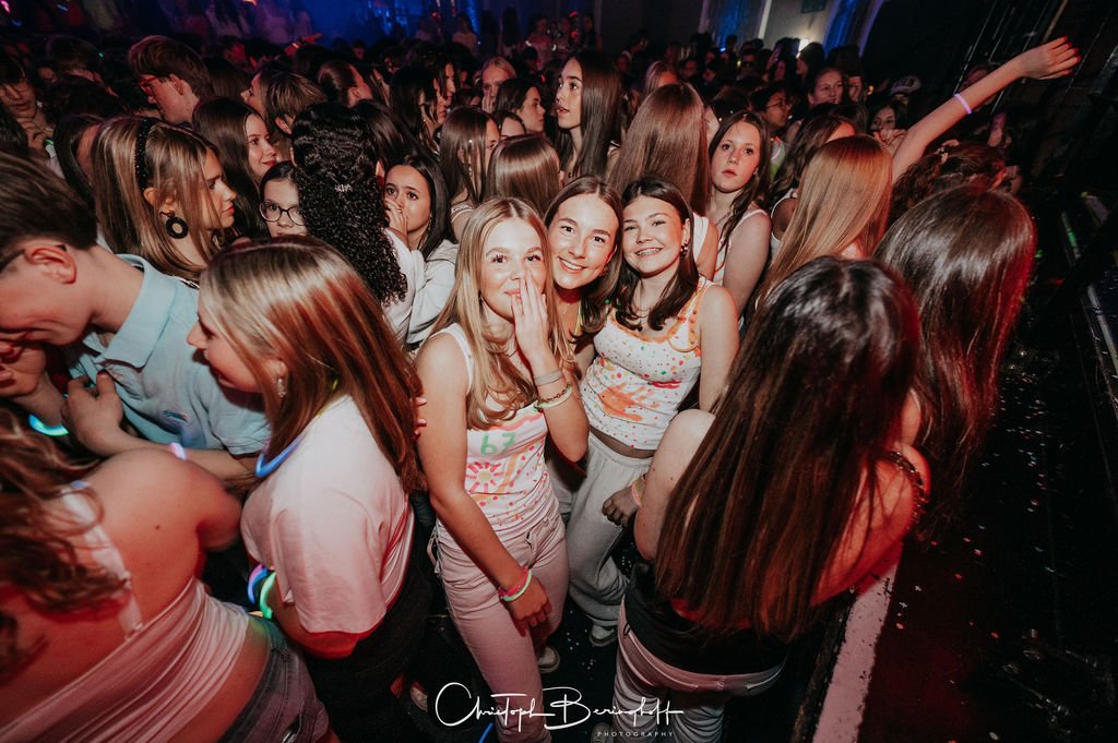 Many teenagers are partying in the dark with colorful lights; some are dancing and laughing.