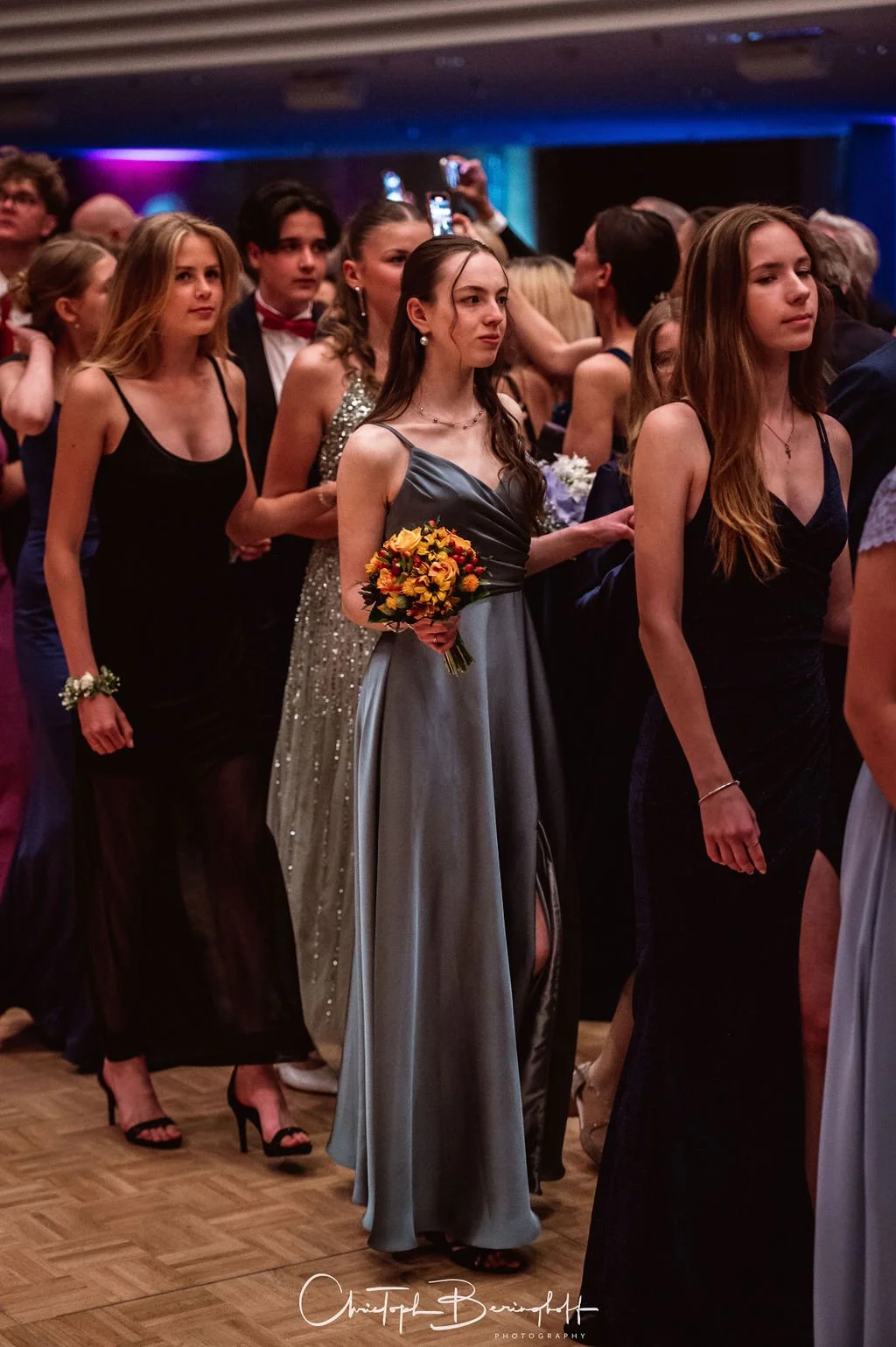 Junge Frauen in eleganten Kleidern bei einer formellen Veranstaltung, eine junge Frau hält einen Blumenstrauß.