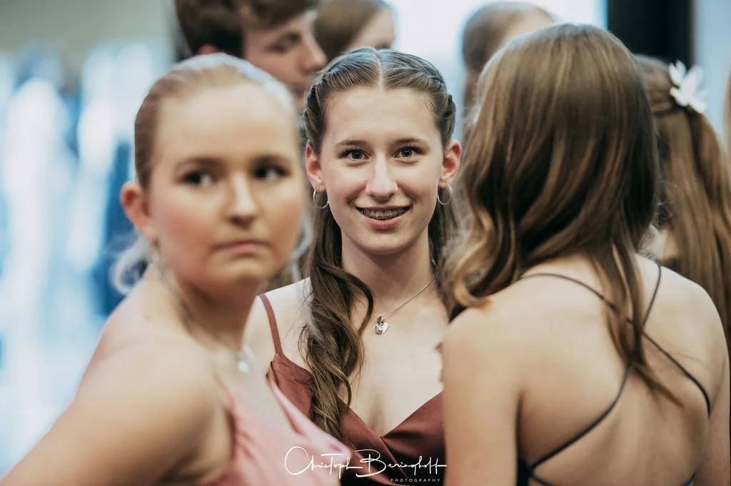 Gruppe junger Frauen bei einer Veranstaltung, eine lächelnde junge Frau im Zentrum, umgeben von anderen Mädchen, die sich unterhalten.
