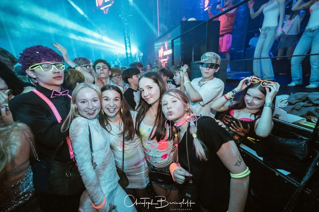 A group of young people at a party or concert in a disco with colorful lights.