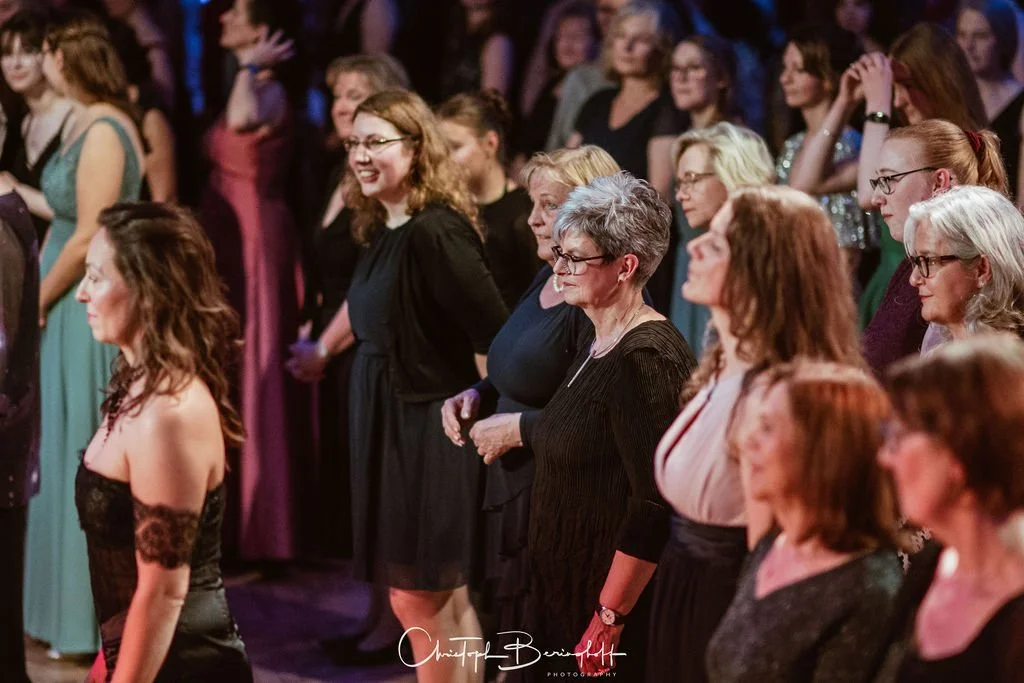 Menschen bei einem festlichen Event, einige stehen im Publikum, einige lachen, in formeller Kleidung.