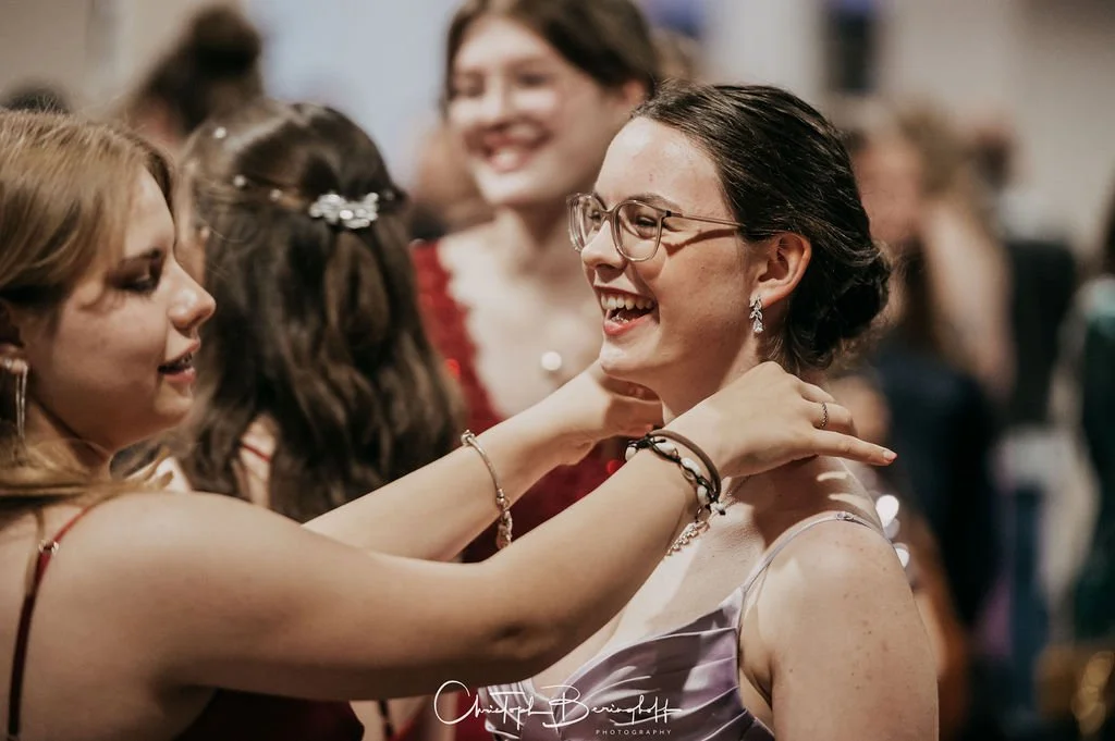 Drei lachende Frauen beim Tanzen auf einer Party, die sich umarmen.