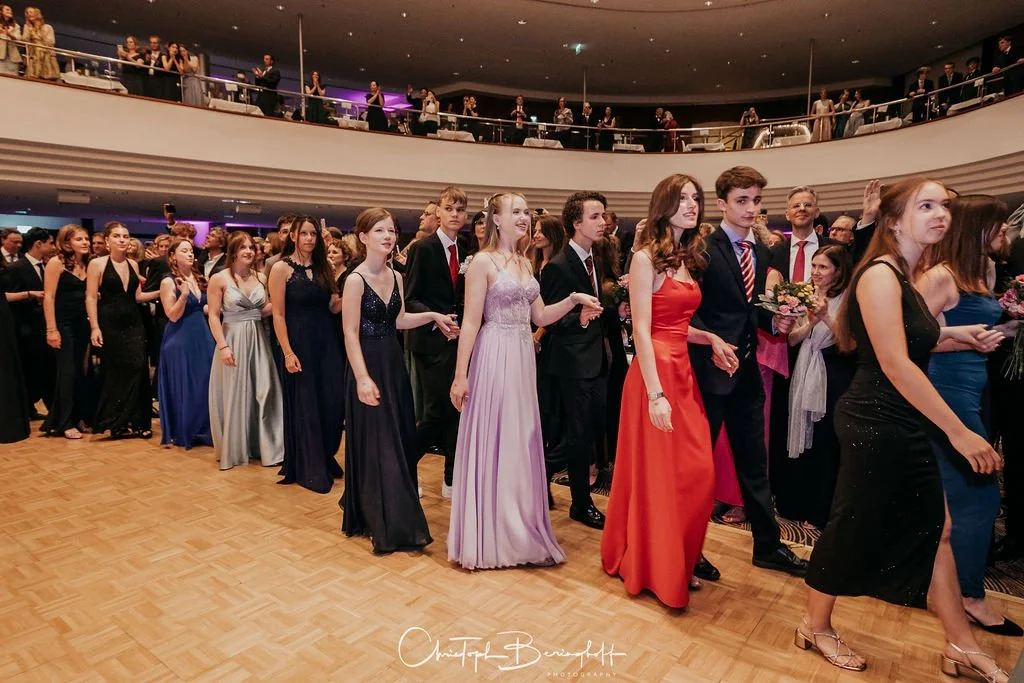 Menschen, die in Abendkleidung bei einer formellen Veranstaltung oder Ball in einem großen Saal tanzen oder sich versammeln.