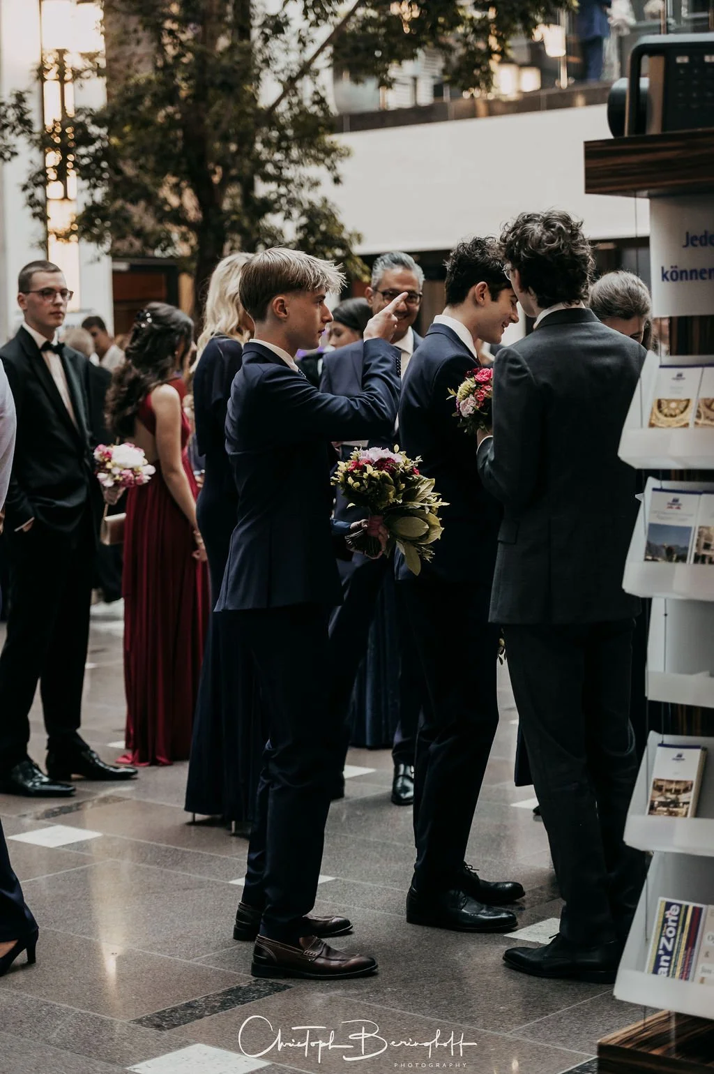Menschen in formeller Kleidung im Gespräch bei einer Veranstaltung, einige halten Blumen. 