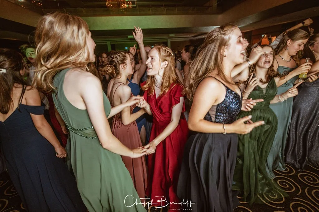 Junge Frauen tanzen und lachen auf einer Party, tragen elegante Kleider.