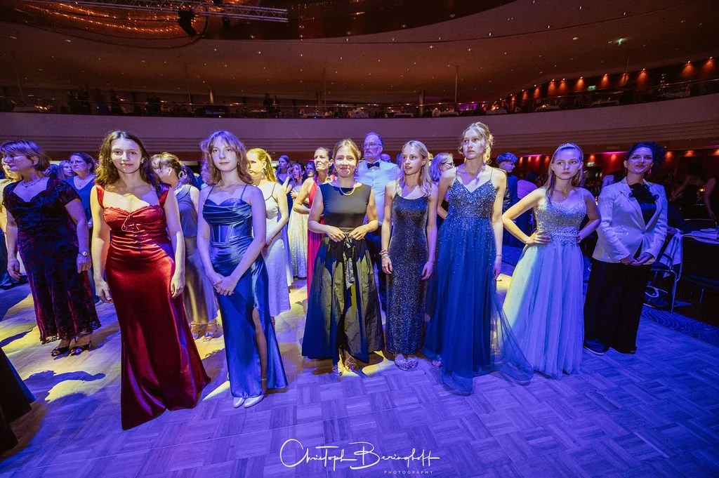 Frauen in eleganten Abendkleidern auf einer Tanzfläche bei einer Feier im Veranstaltungsraum.