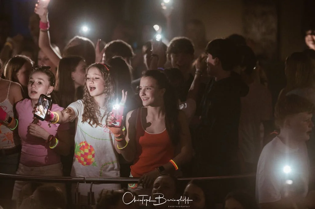 Teenagers at a party wearing glow-in-the-dark wristbands; some are taking photos or videos, while others are having fun and laughing.