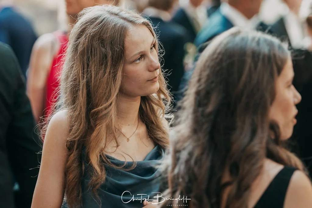 Jugendliches Mädchen mit braunen, lockigen Haaren bei einer formellen Veranstaltung.
