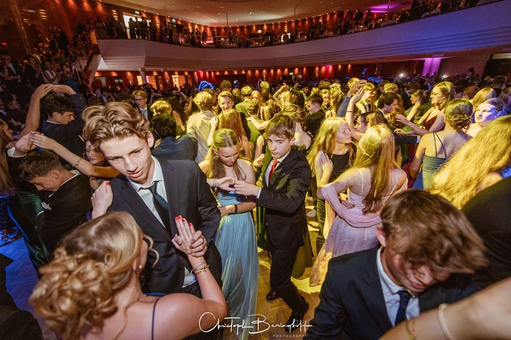 Menschen tanzen auf einem information- und lichtgefüllten Ball in formeller Abendkleidung.