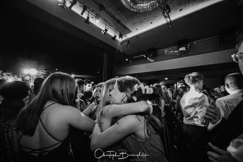 Menschen tanzen und umarmen sich auf einer Feier in einem großen Veranstaltungsraum, schwarz-weiß Fotografie.