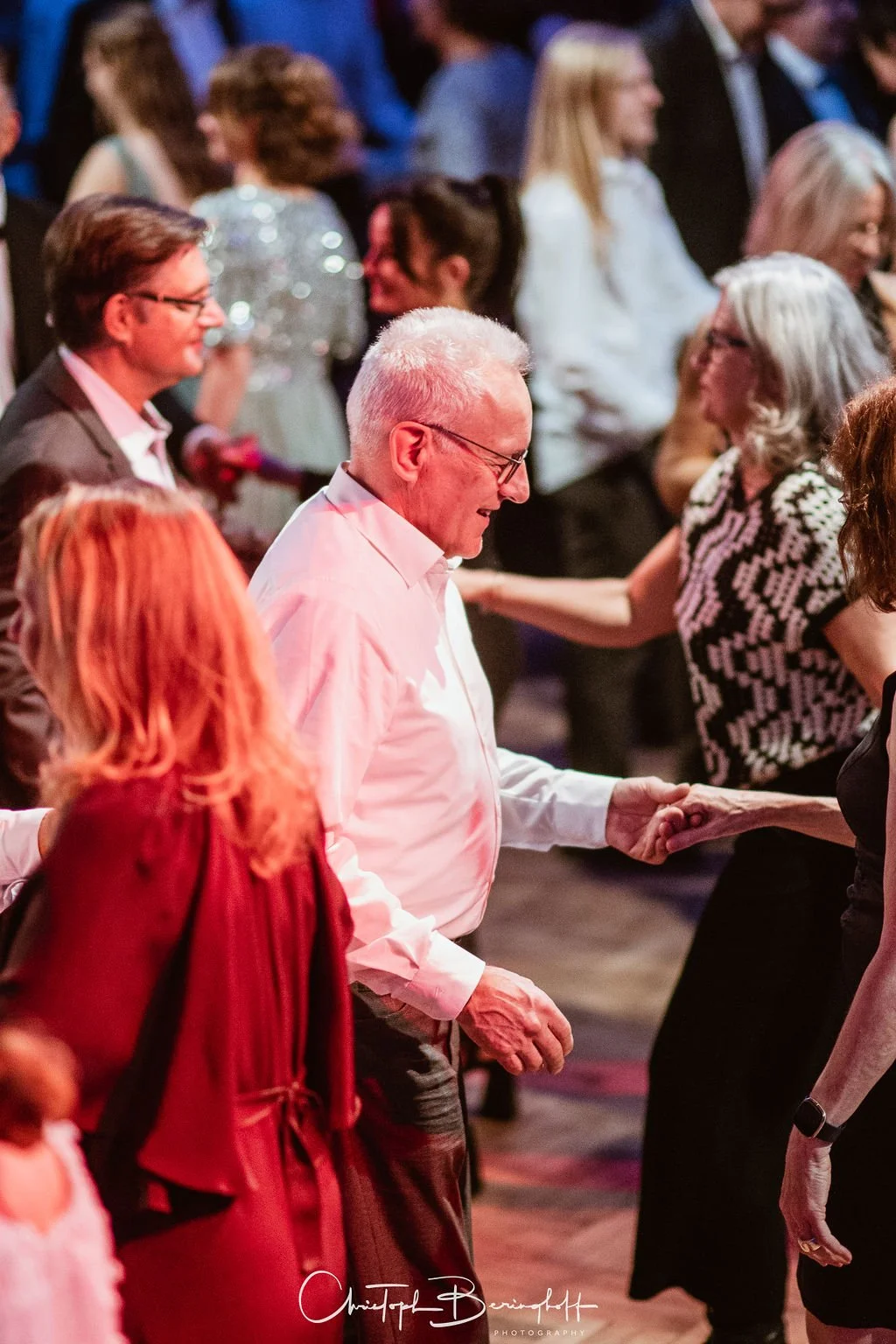 Ältere Männer und Frauen tanzen und feiern bei einer Veranstaltung, in einer fröhlichen Atmosphäre.