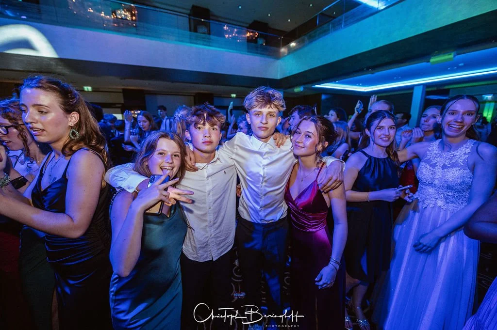 Gruppe junger Menschen bei einer Party, tanzen und lachen in einem Raum mit blauer Beleuchtung.