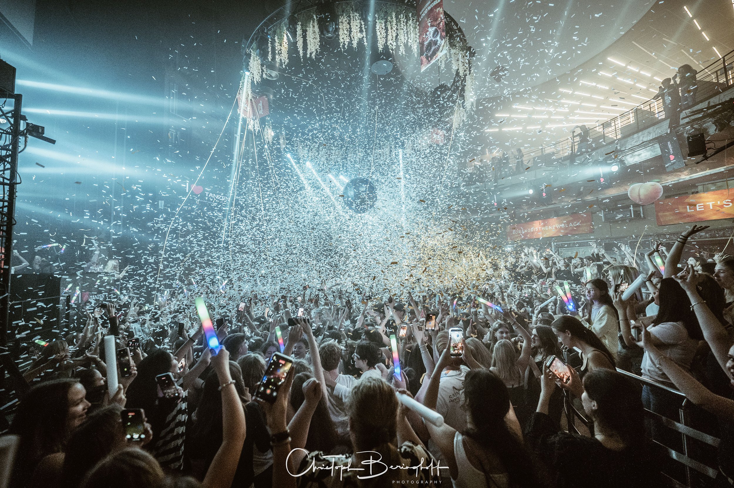Menschen feiern bei einer Party im dunklen Raum mit Konfetti, Discokugel und Lichteffekten, während sie mit ihren Handys Fotos machen.