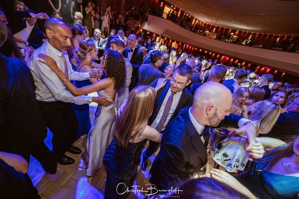 Tanzpaar auf einem festlichen Ball, viele Menschen tanzen fröhlich, elegante Kleidung, festliche Atmosphäre.