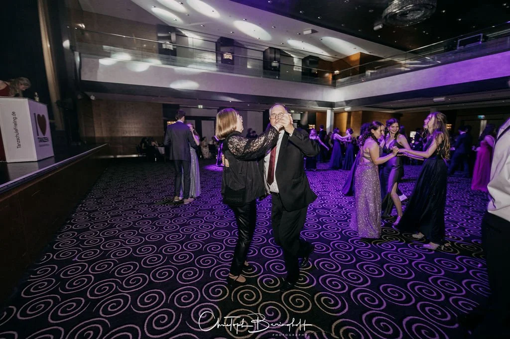 Menschen tanzen auf einer Party im Ballsaal, mange im Hintergrund, elegante Kleidung.
