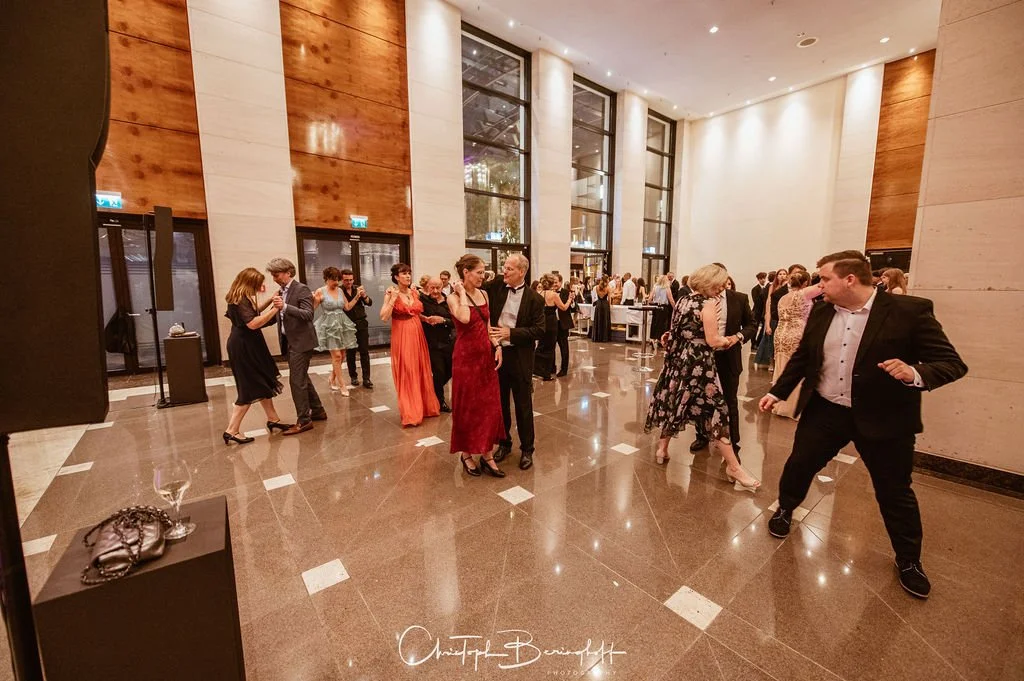 Menschen tanzen auf einer eleganten Feier in einem großen stilvollen Saal mit hohen Fenstern und modernem Design.